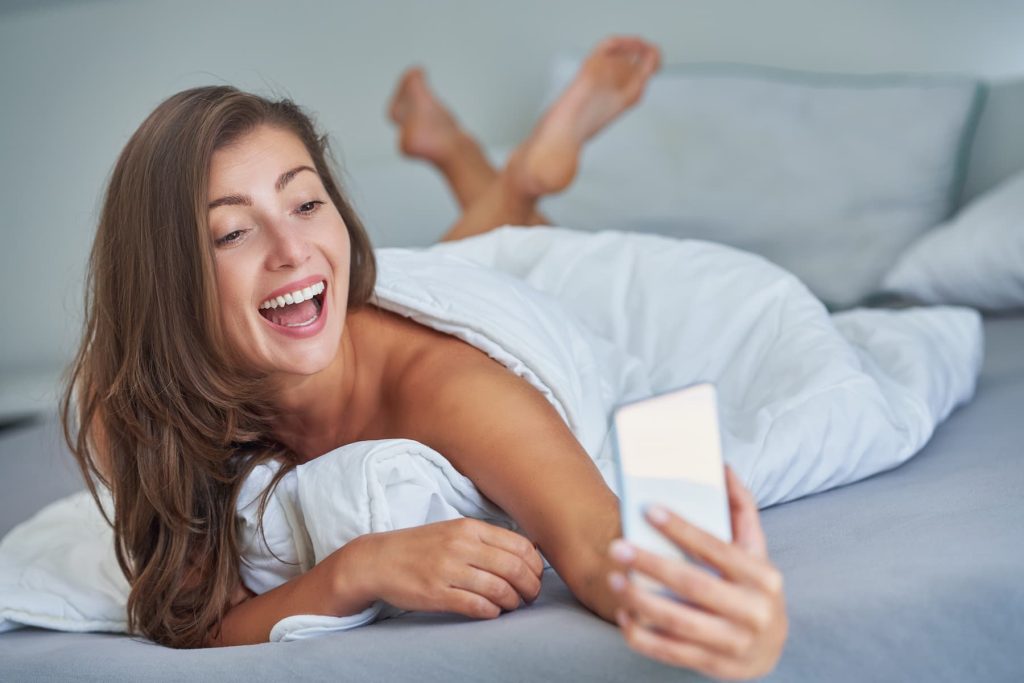 Fille sexy brune sur le lit avec téléphone souriant.